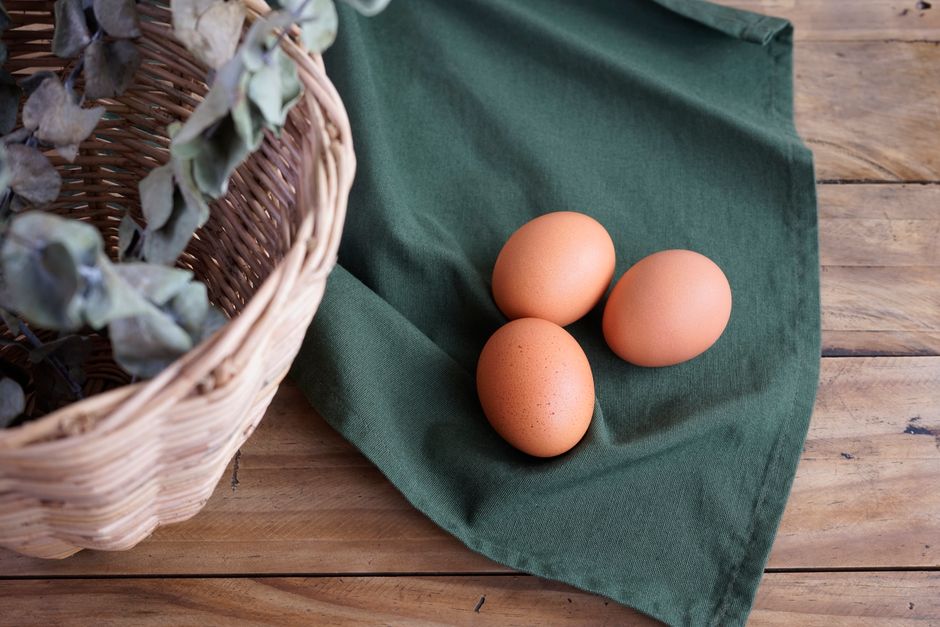 Friss tojás és farmi kosarak faasztalon, zöld mezővel a háttérben